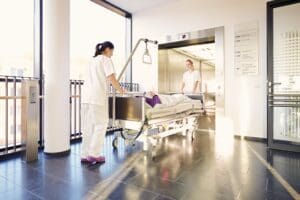 Two nurses pushing a patient into a lift within a hospital building