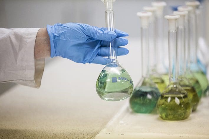 A scientist in a lab coat carefully holds a beaker containing liquid, conducting an experiment in a laboratory setting.